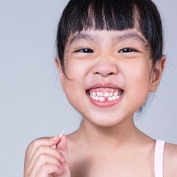 child smiling while holding a tooth they lost