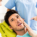 Male patient in dental chair holding cheek in pain